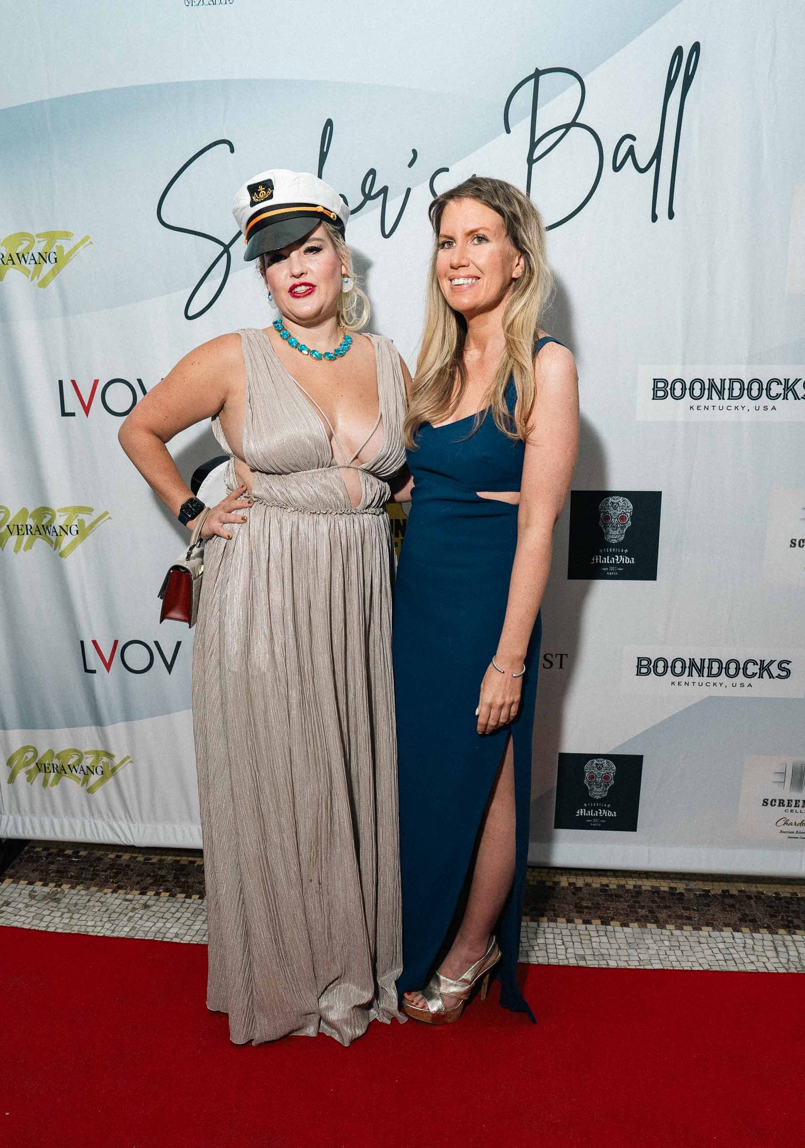 Two women in elegant gowns at Sailor's Ball 2024 photo wall New York City